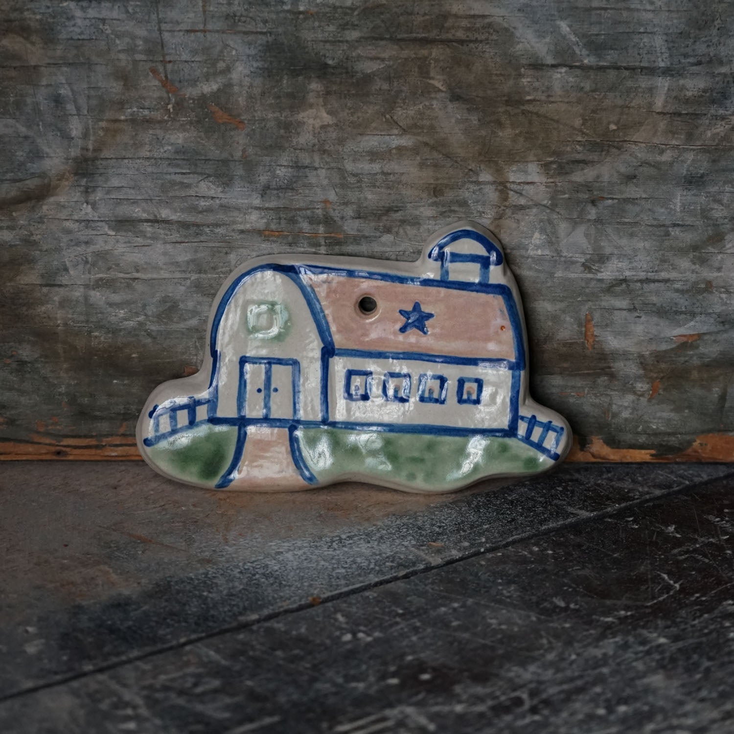 Ceramic barn-shaped ornament with blue and white design on a rustic wooden background