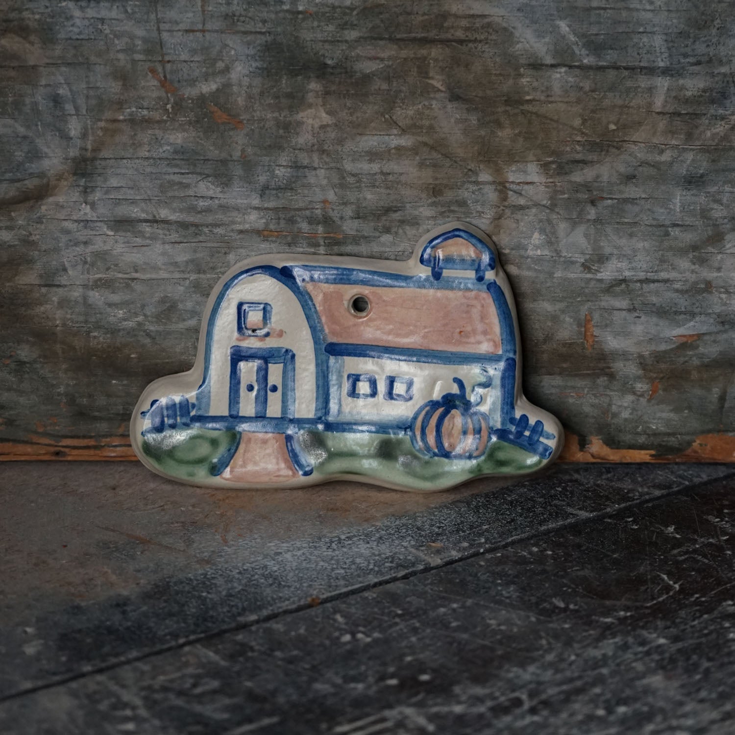 Ceramic tile with a barn and pumpkin design on a rustic wooden surface